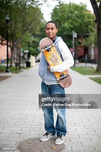 teen boy holding skateboard on urban street - boy skating stock pictures, royalty-free photos & images