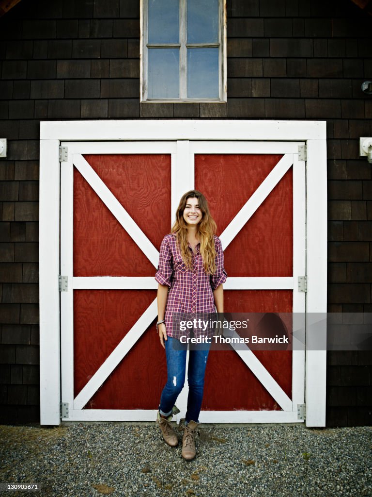 Young woman standing in front of barn smiling