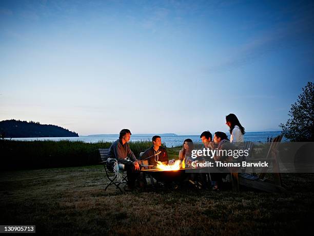 group of friends roasting hot dogs at dusk - lagerfeuer stock-fotos und bilder