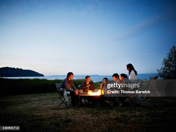 group of friends roasting hot dogs at dusk - camping campfire stock pictures, royalty-free photos & images