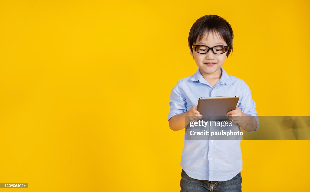 Portrait of little Asian boy with smartphone with copy space on yellow background. Success and happy toddler boy, education technology concept