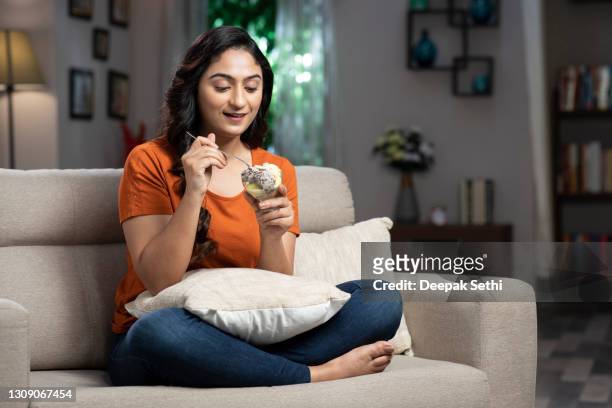 shot of a young woman eating icecream sundae at home:- stock photo - mulher colher sorvete imagens e fotografias de stock