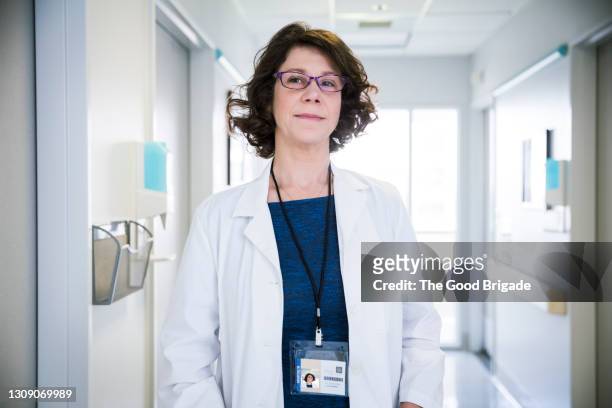 portrait of confident mature doctor standing in hospital corridor - ネックストラップ ストックフォトと画像