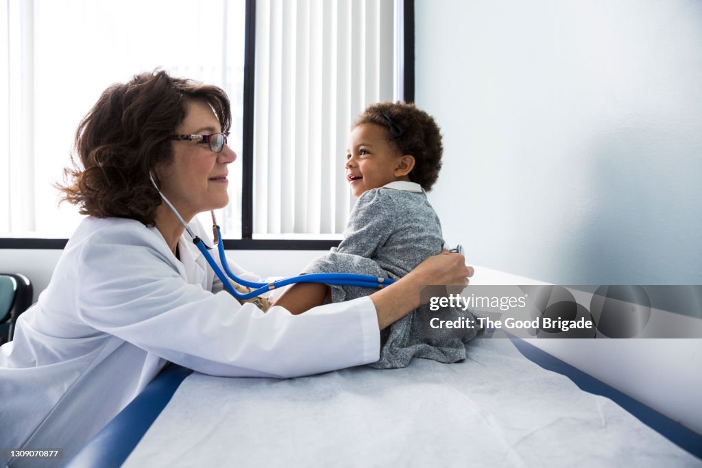 Smiling pediatrician examining baby girl with stethoscope