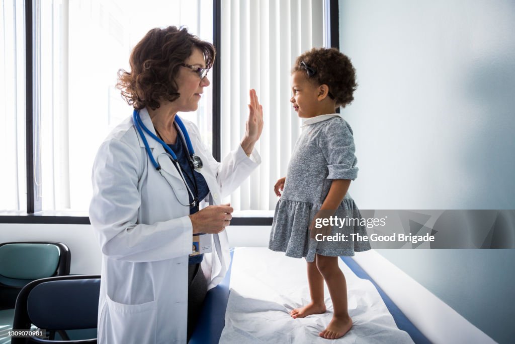 Female pediatrician giving high-five to baby girl in hospital