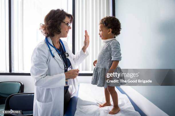 female pediatrician giving high-five to baby girl in hospital - girl side view stockfoto's en -beelden