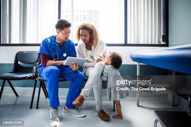 male nurse showing digital tablet to mother by toddler in hospital - gezondheidszorg en medicijnen stockfoto's en -beelden