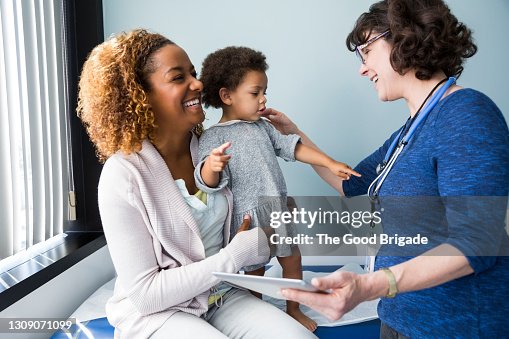 Smiling pediatrician showing digital tablet to mother and baby in exam room