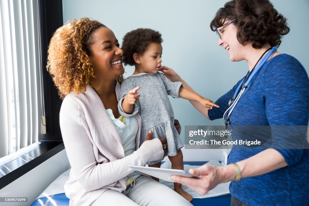 Smiling pediatrician showing digital tablet to mother and baby in exam room