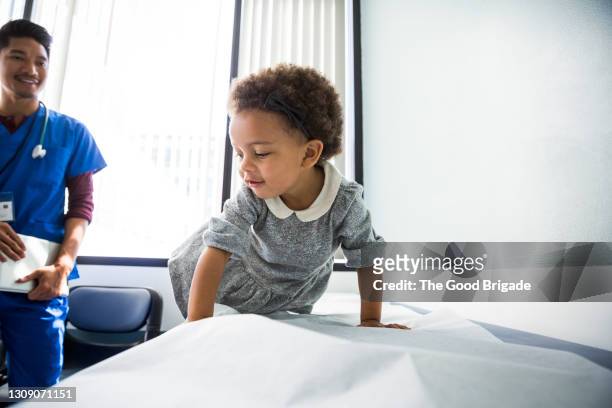 smiling toddler sitting on examination table in doctors office - naughty nurse images stock-fotos und bilder
