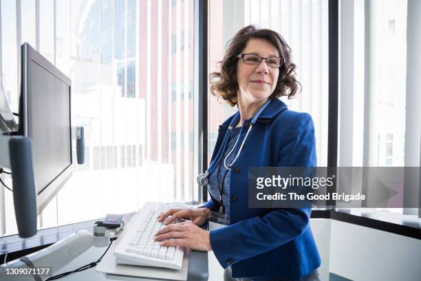 smiling female doctor working on computer in hospital - blue blazer stock pictures, royalty-free photos & images