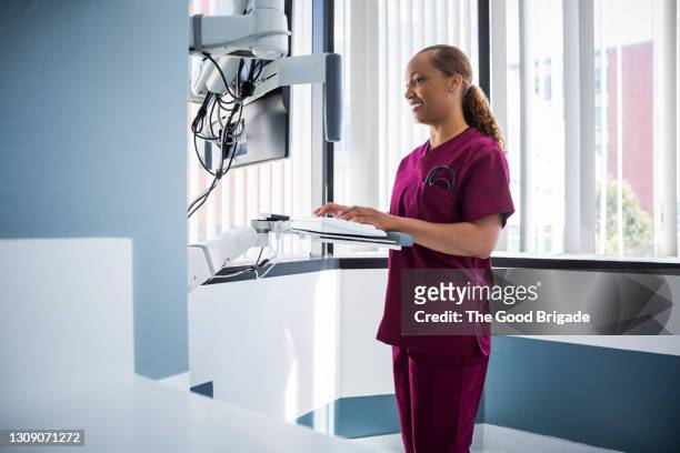 smiling female nurse working on computer in hospital - nurse maroon stock pictures, royalty-free photos & images