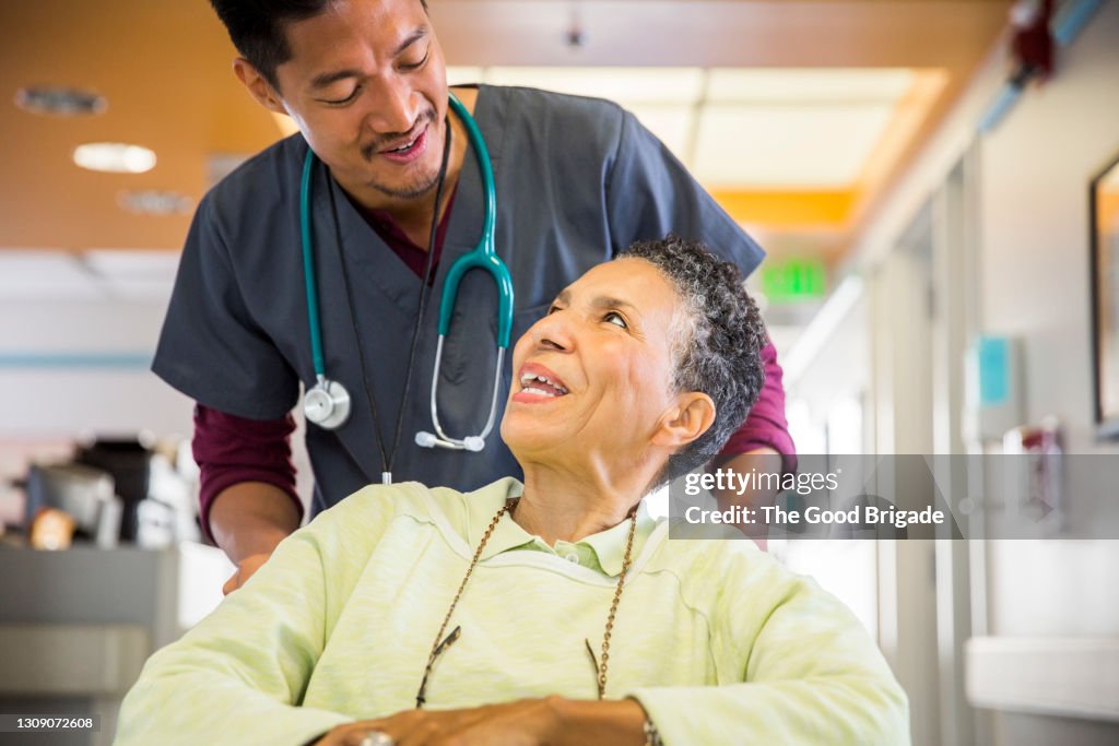 Male nurse pushing cheerful senior woman in wheelchair
