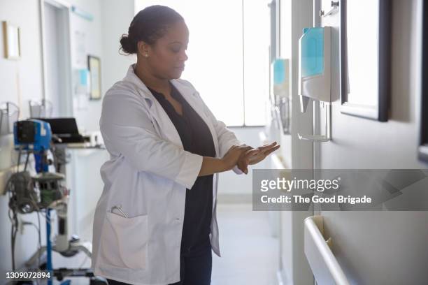 female doctor using hand sanitizer in hospital corridor - gel antiséptico fotografías e imágenes de stock