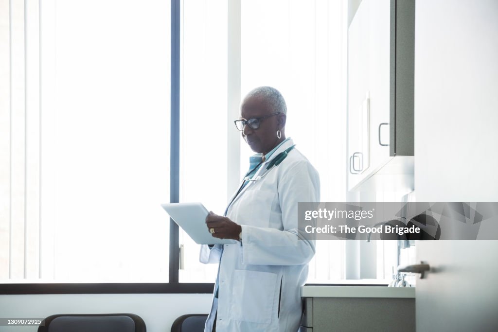 Doctor reviewing medical chart on digital tablet in exam room