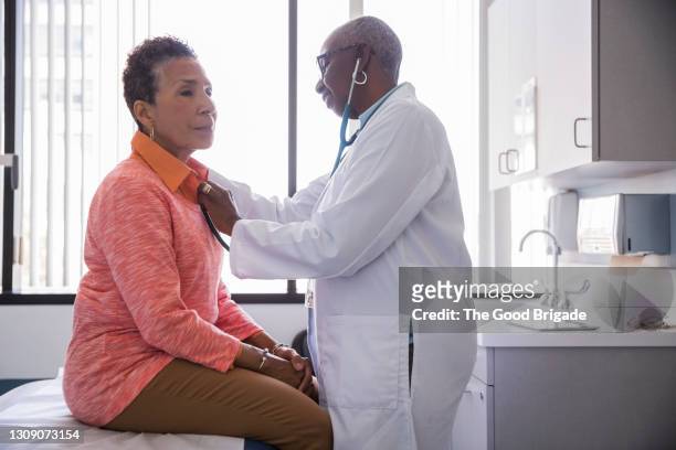 smiling female doctor examining senior patient in hospital - doctors fotografías e imágenes de stock
