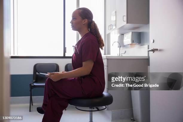 female nurse with digital tablet sitting in hospital exam room - nurse maroon stock pictures, royalty-free photos & images