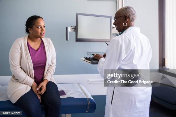 smiling senior doctor talking to patient in hospital - tavolo da visita foto e immagini stock