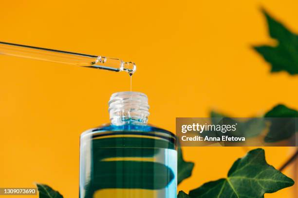 drop of hyaluronic acid is falling directly into blue glass bottle on illuminating yellow background with blurred green leaves. concept of natural cosmetics and organic components with vitamin c. trendy colors of the year 2021. close-up front view - cbd products stock pictures, royalty-free photos & images