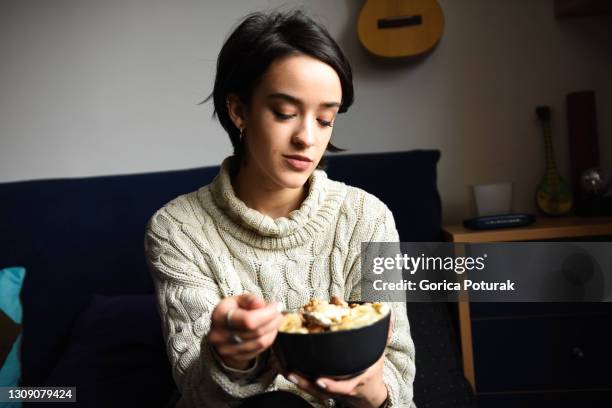 schöne junge frau im wohnzimmer essen müsli mit haselnüssen und bananen - eating nuts stock-fotos und bilder