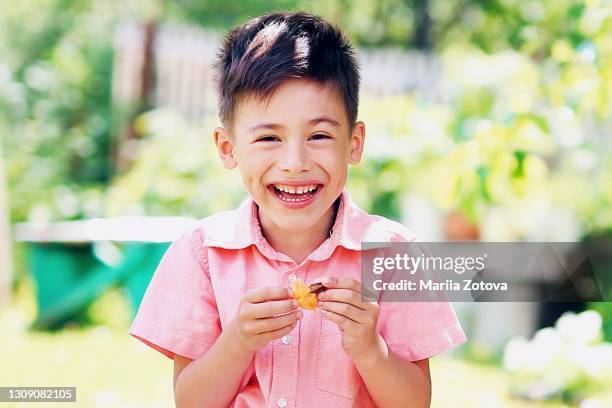 little boy is smiling in the nature, outdoors and eating fruit. - giorno dei bambini foto e immagini stock