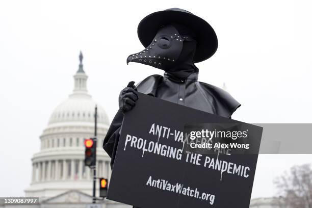 Man holds a sign and dresses as a plague doctor to encourage people to be vaccinated and prevent prolonging the COVID-19 pandemic March 25, 2021 on...