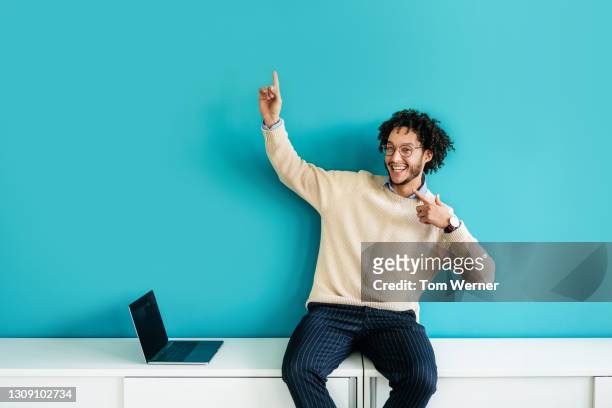 office employee pointing while sitting on cabinet - portrait of man smiling black jumper stock-fotos und bilder