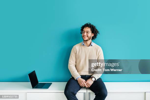 cheerful office employee sitting on cabinet smiling - fondo color fotografías e imágenes de stock