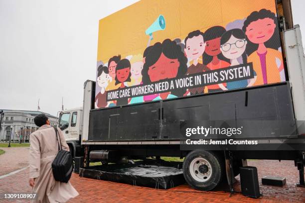 Commuters and Congressional staff walk past an LED display during a protest calling on Congress to invest in Care jobs at Union Station on March 25,...