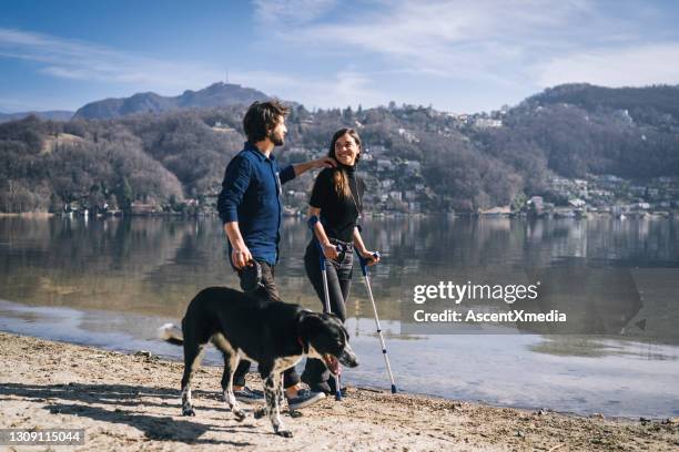 couple walk with their dog by lakeshore in the morning - crutch stock pictures, royalty-free photos & images