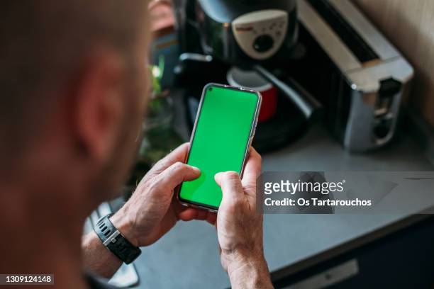 man holding a green screen smart phone with both handsand using thumbs while making a coffee - man holding phone imagens e fotografias de stock