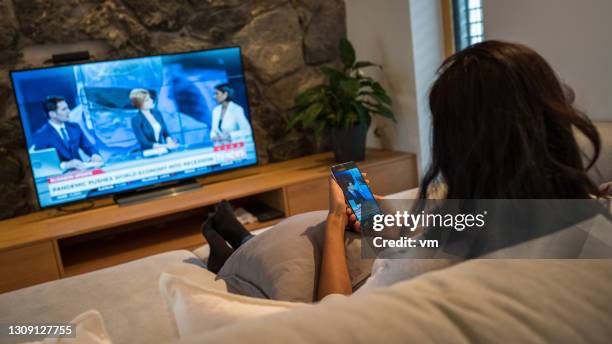 mujer sentada en la sala de estar y viendo las noticias transmitidas - acontecimientos en las noticias fotografías e imágenes de stock