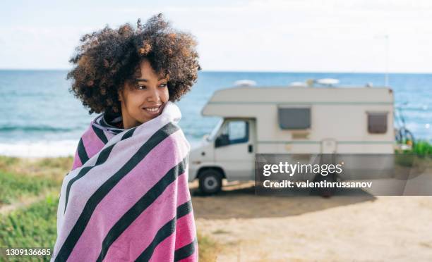 glimlachende afrovrouwen die met een strandlaken wordt verpakt dat van haar zomervakantie met camper geniet - strandhanddoek stockfoto's en -beelden