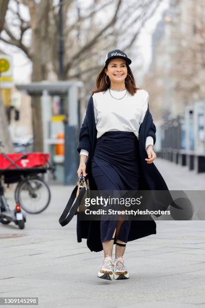 Model and DJane Gitta Saxx wearing a white sweater pullover by Sonja Kiefer Studio, a dark blue wrap skirt by Sonja Kiefer Studio, a dark blue and...