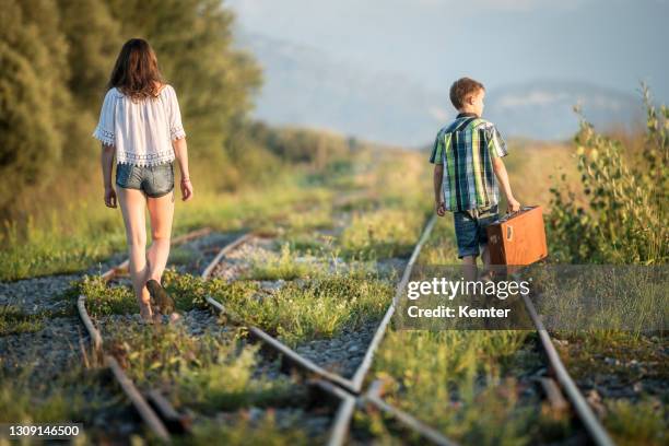 niña y niño con bolsa caminando por las vías - fugitive fotografías e imágenes de stock