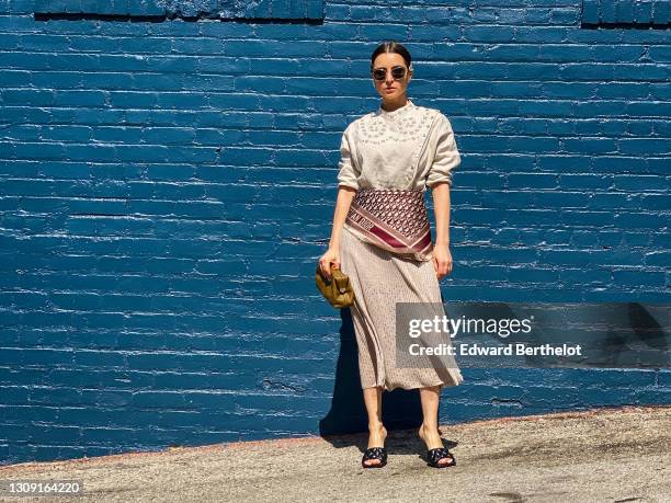 Julia Comil wears a hair clip, sunglasses, a beige eyelet blouse in linen by Carven, a beige Midi skirt by Carven, a Dior silk scarf with printed...