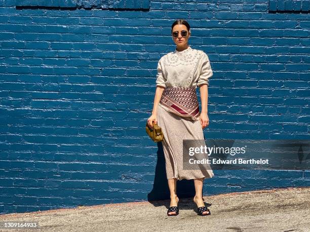 Julia Comil wears a hair clip, sunglasses, a beige eyelet blouse in linen by Carven, a beige Midi skirt by Carven, a Dior silk scarf with printed...