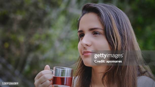 head shot close-up of hispanic young woman drinking a cup of hibiscus hot tea at outdoors terrace - real time stock pictures, royalty-free photos & images