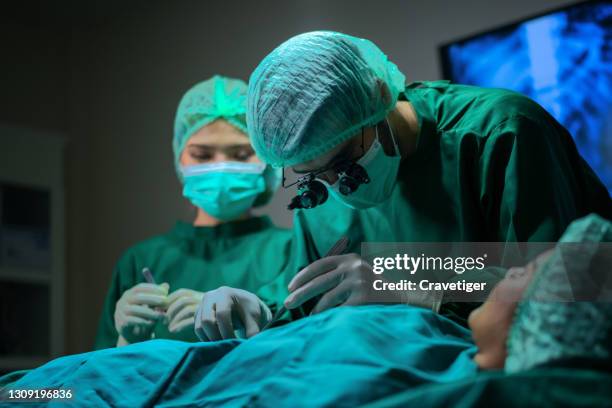 surgeons operating patient for breast implant. team of doctors are in scrubs at operating room. - transplant surgery stock-fotos und bilder