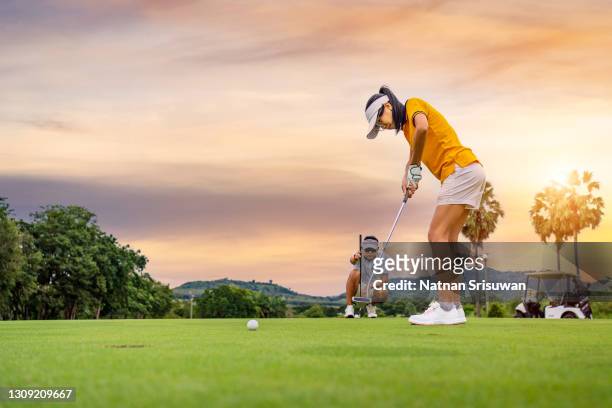 man teaching woman to play golf while standing on field - golf putter stock pictures, royalty-free photos & images