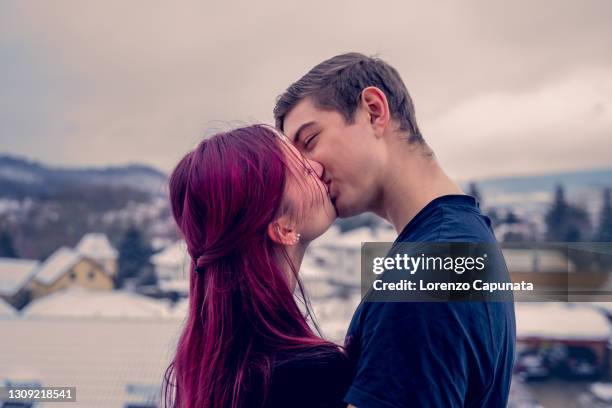 young couple kisses on the balcony of their new home. in the background the snowy landscape. - teenagers kissing stock pictures, royalty-free photos & images