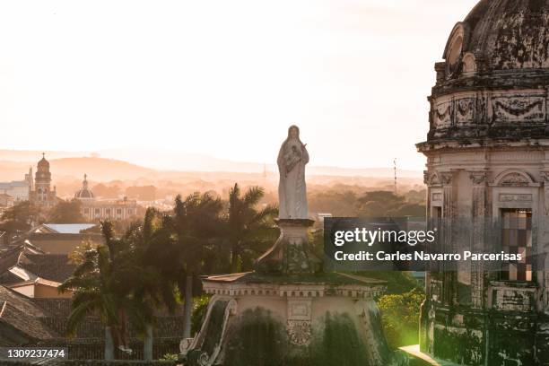 statue and dome of the church of la merced with the church of xalteva in the background during sunset. granada, nicaragua - nicaragua stock-fotos und bilder