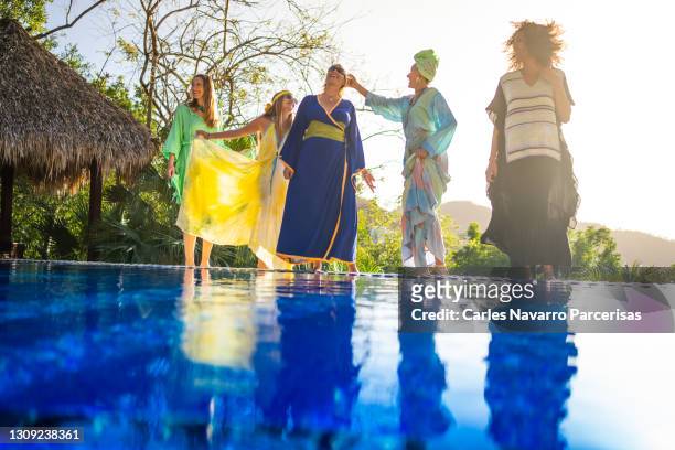 women of different ethnicities in dresses dancing and joking on the edge of a swimming pool with the sun shining on them at sunset - central america stock pictures, royalty-free photos & images