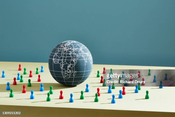 a world globe surrounded by people figurines - emigration and immigration stock pictures, royalty-free photos & images