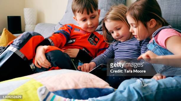 three children reading on a sofa - family with three children fotografías e imágenes de stock