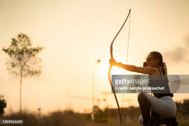 rear view of sportswoman doing archery on a sports field against sunset . - natural shot female stock pictures, royalty-free photos & images