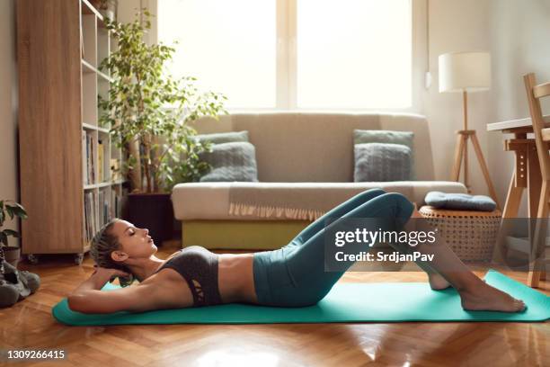 zijaanzicht van een vrouw in sportkleding die thuis op haar mat praktiseert - sit ups stockfoto's en -beelden