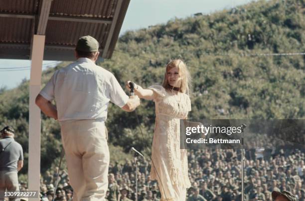 British-born American comedian Bob Hope passes the microphone to American singer and actress Gloria Loring at the Christmas show staged for troops at...