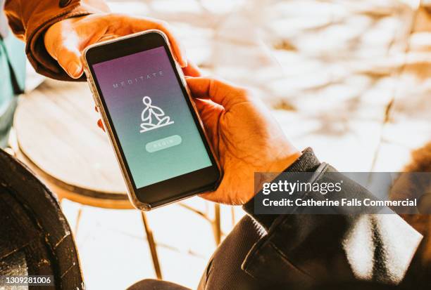 hand holding a smart phone that displays a meditation app - peaceful demonstration stock pictures, royalty-free photos & images