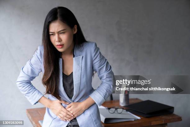 unhealthy young asian businesswoman with stomachache in office. - diarrhoea foto e immagini stock